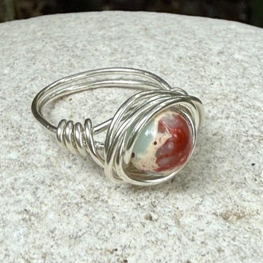 Silver wire-wrapped ring with a sea sediment jasper on a textured surface