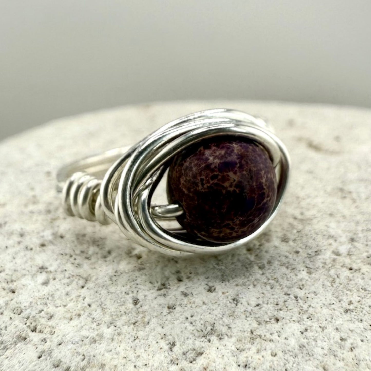 Silver wire-wrapped ring with a purple stone on a textured surface