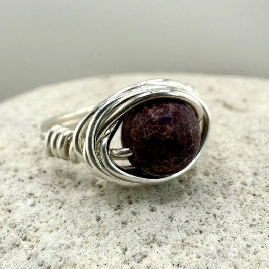 Silver wire-wrapped ring with a purple stone on a textured surface