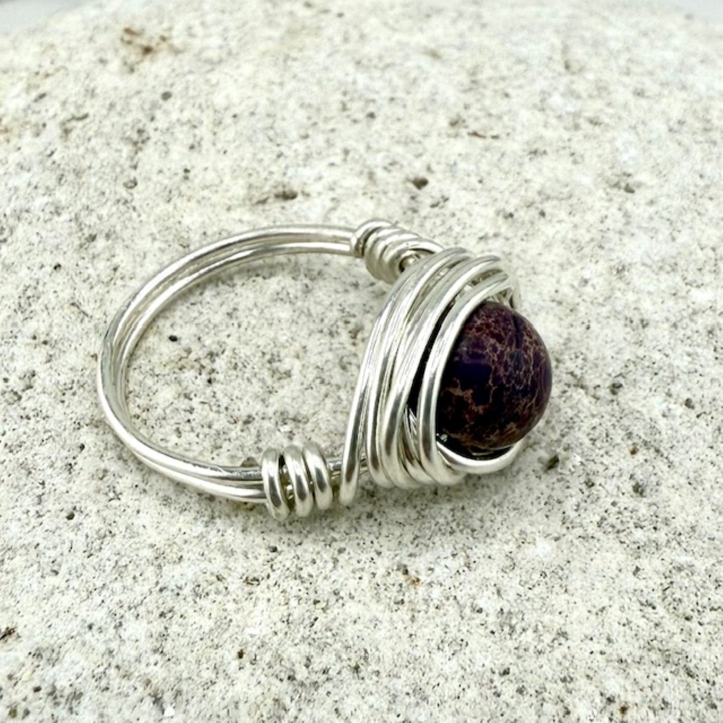 Silver wire-wrapped ring with a purple stone on a stone background