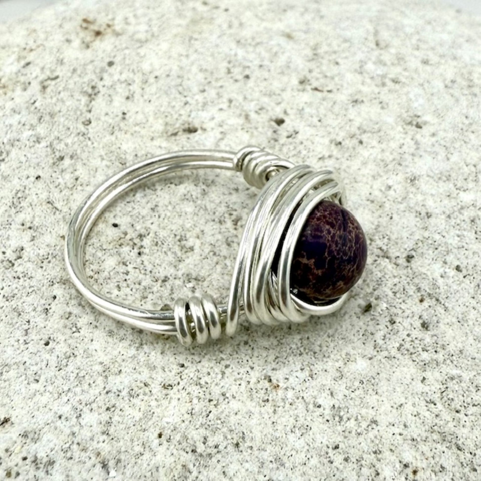 Silver wire-wrapped ring with a purple stone on a stone background