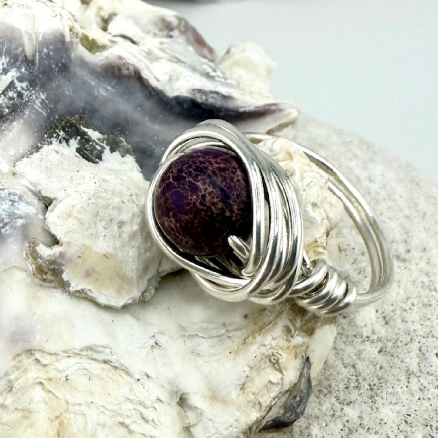 Silver wire-wrapped ring with a purple stone on a shell