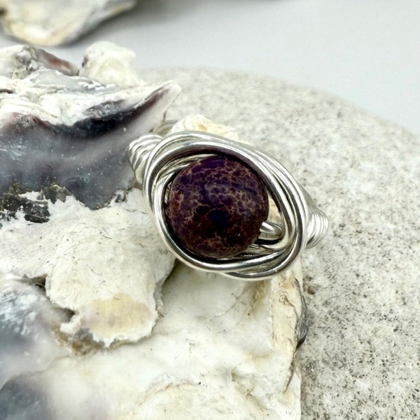 Silver wire-wrapped ring with a purple stone on a textured surface