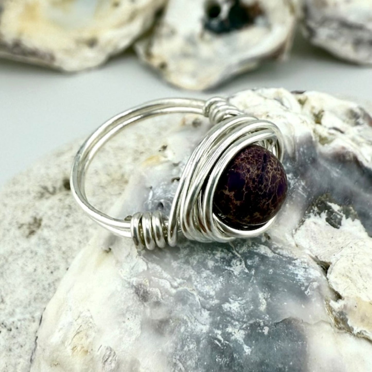 Silver wire-wrapped ring with a purple stone on a textured surface