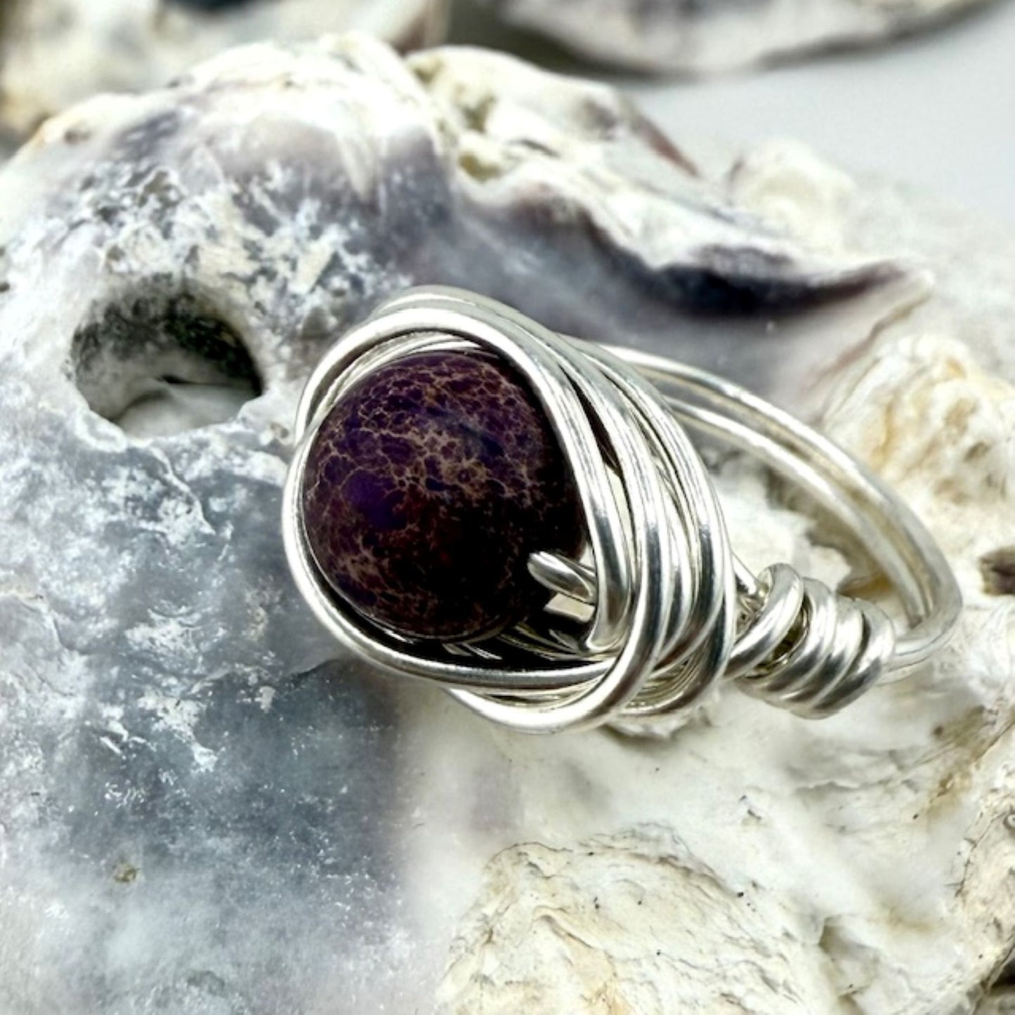 Silver wire-wrapped ring with a purple stone on a textured stone background
