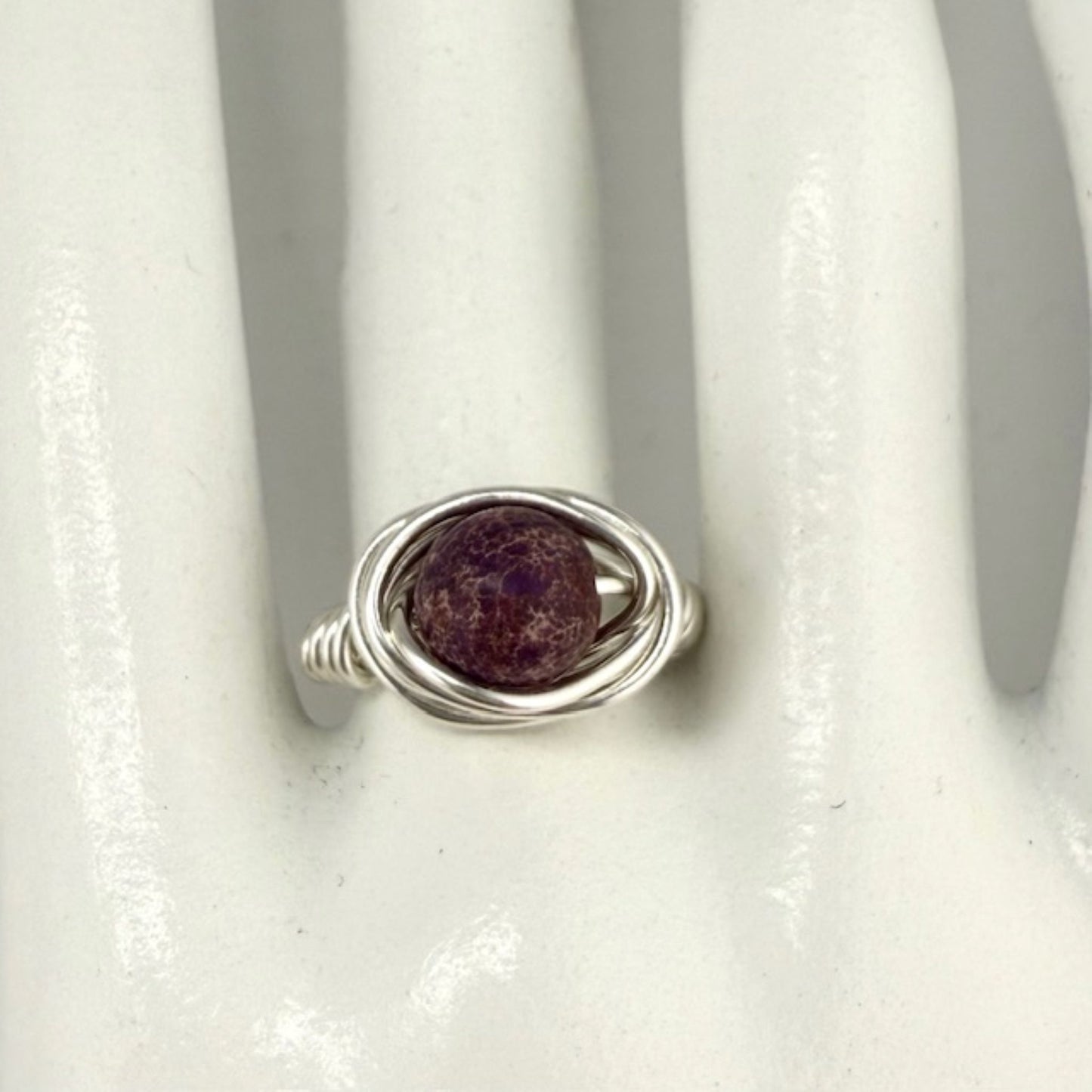 Silver ring with a purple stone on a white display hand
