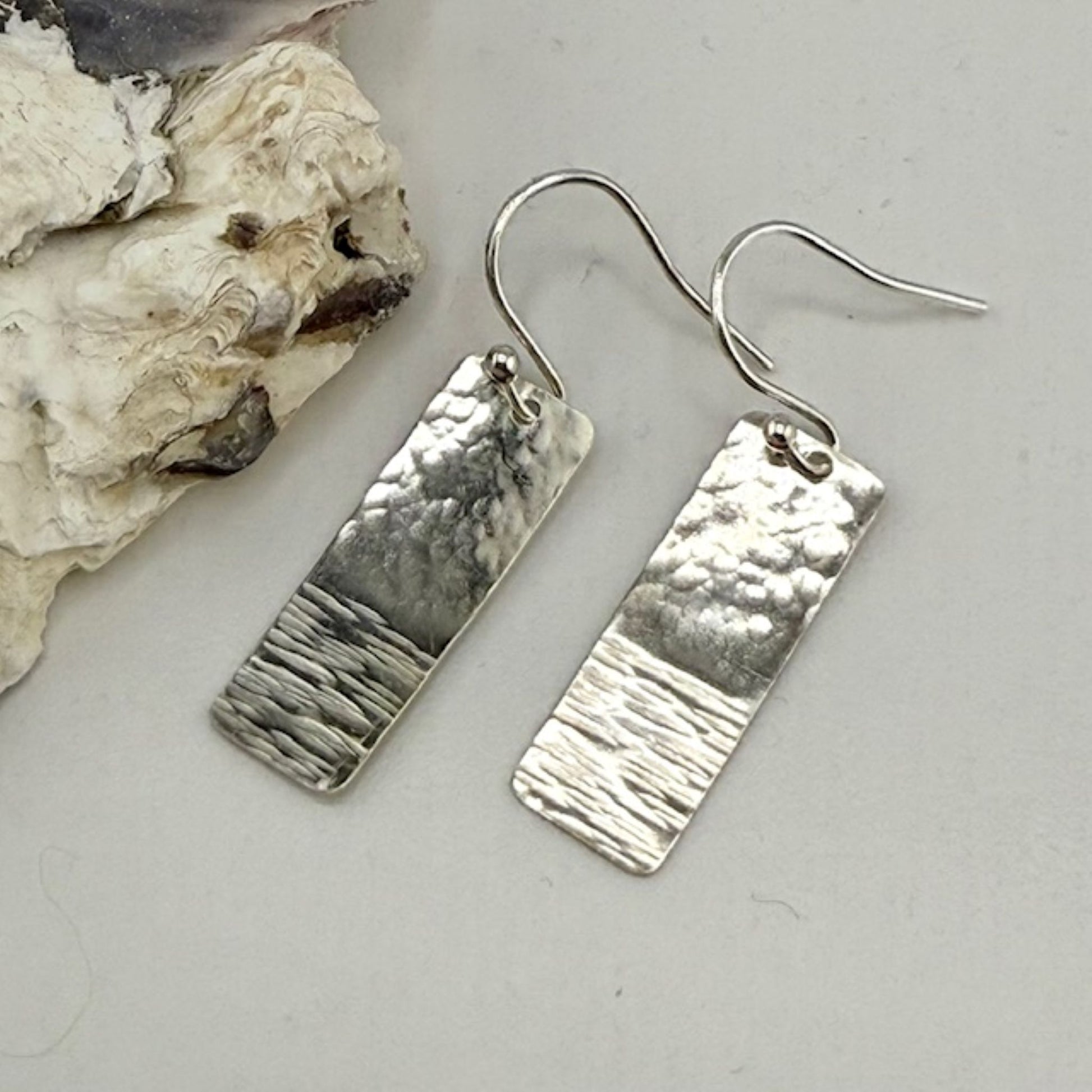 Pair of silver rectangle earrings on a textured stone surface
