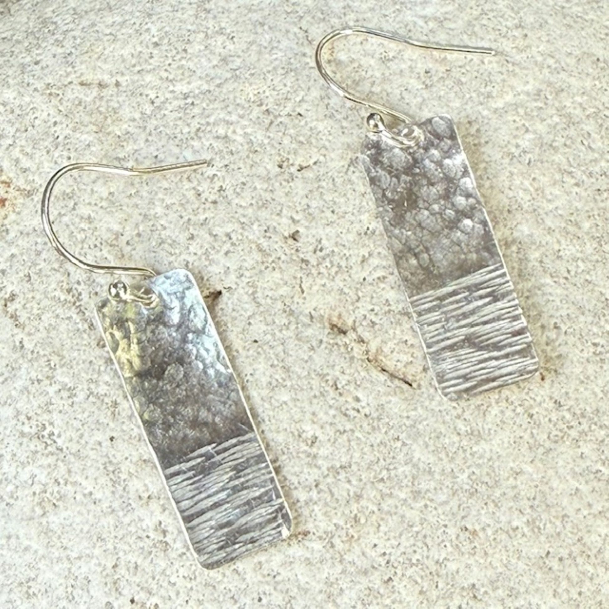 Pair of silver bar earrings on a textured stone surface