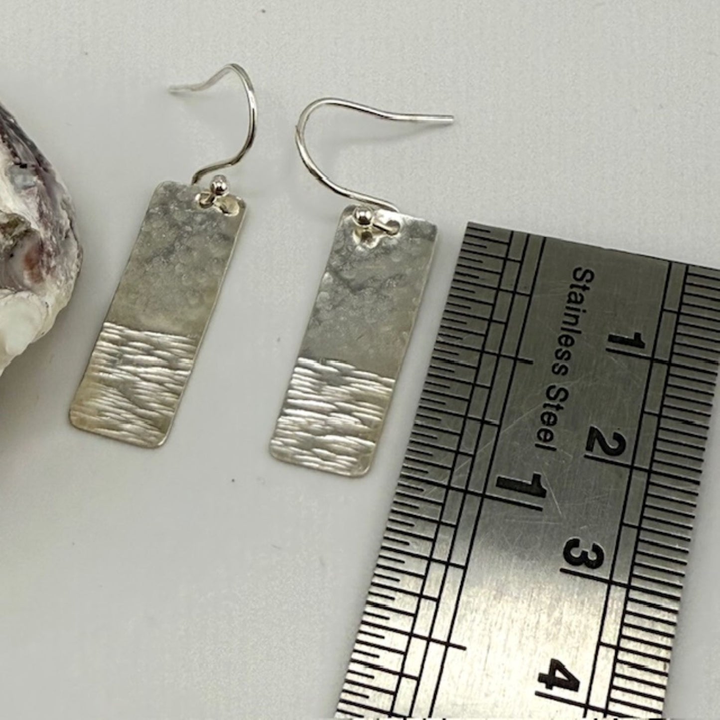 Silver textured bar earrings with a ruler for scale on a white background