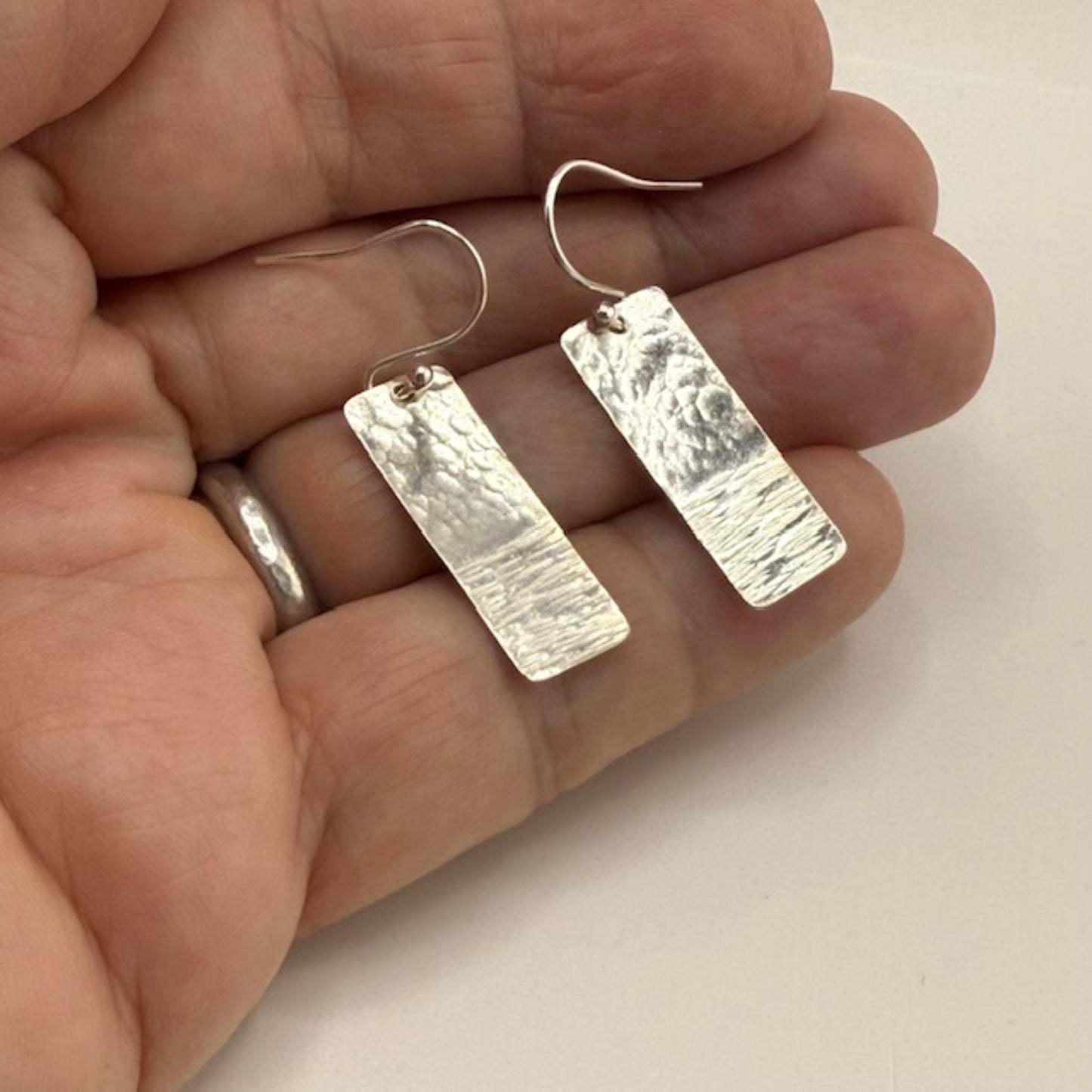 Textured silver bar earrings being held in a human hand