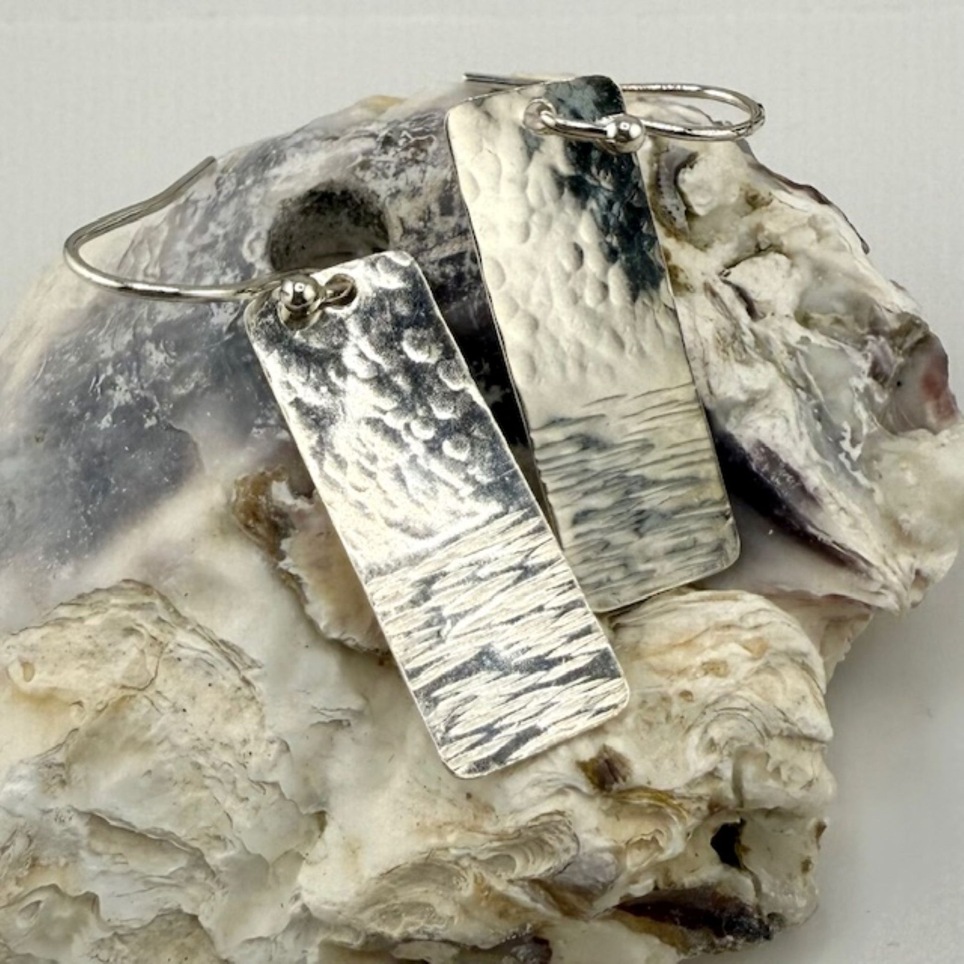 Silver bar rectangle earrings on a textured stone surface