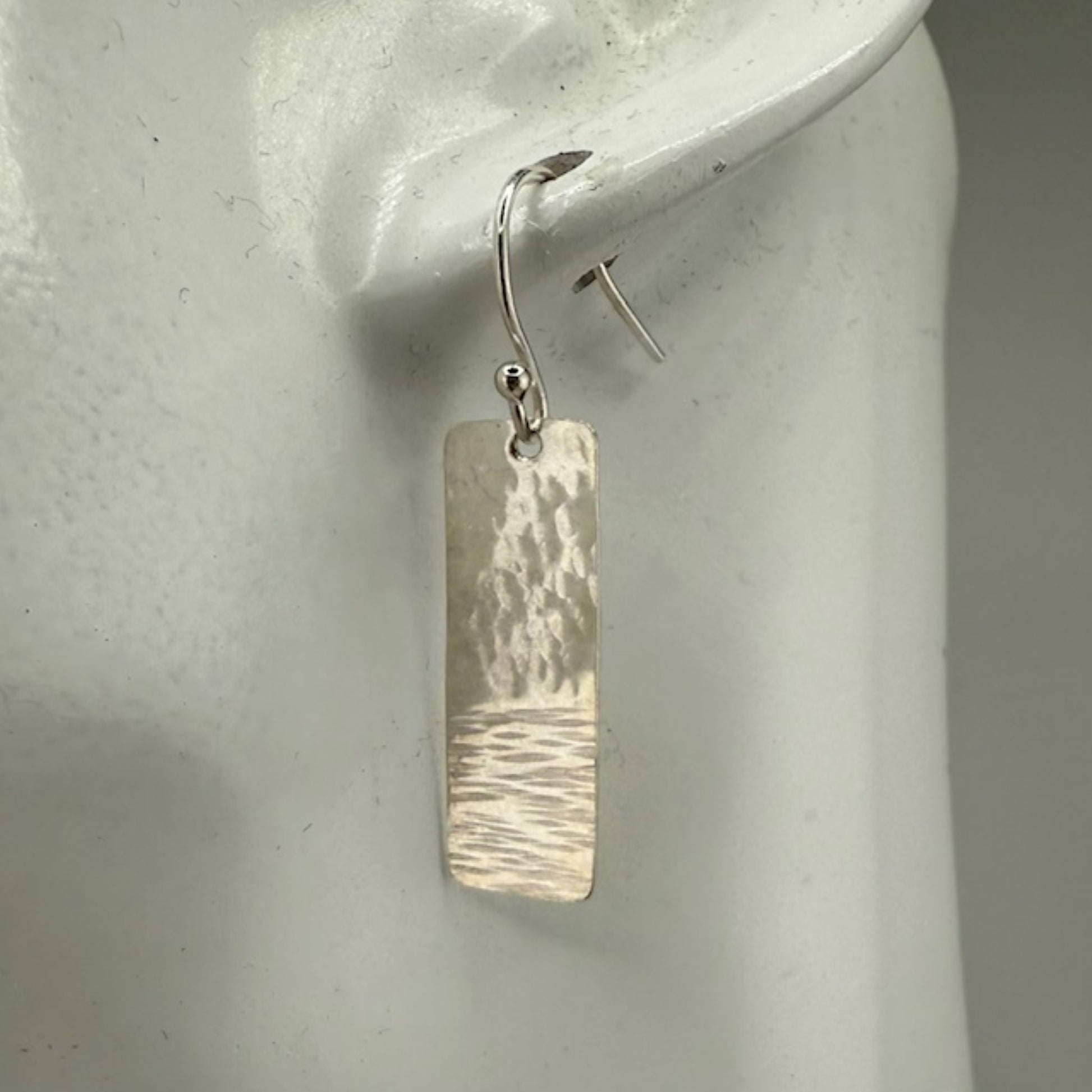 Silver bar earrings on a white mannequin ear