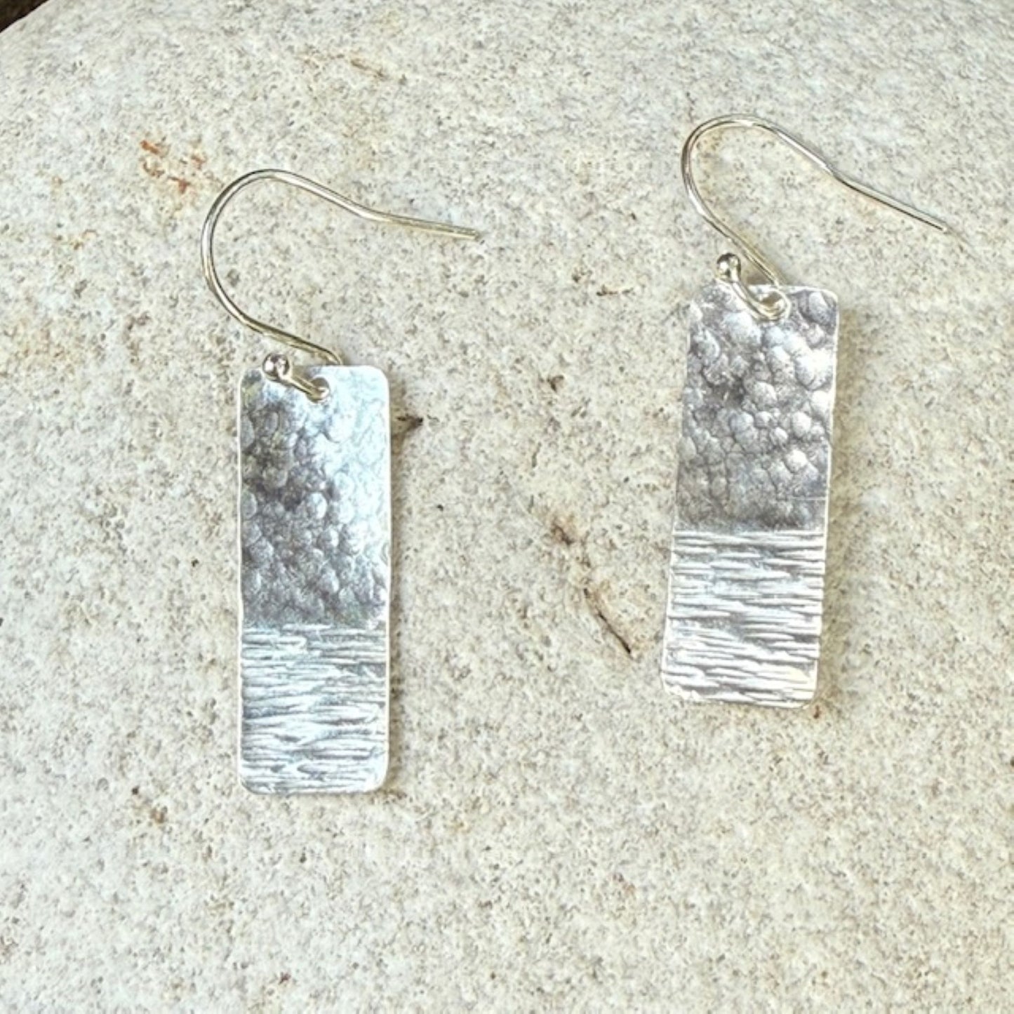 Silver rectangular earrings on a textured stone surface