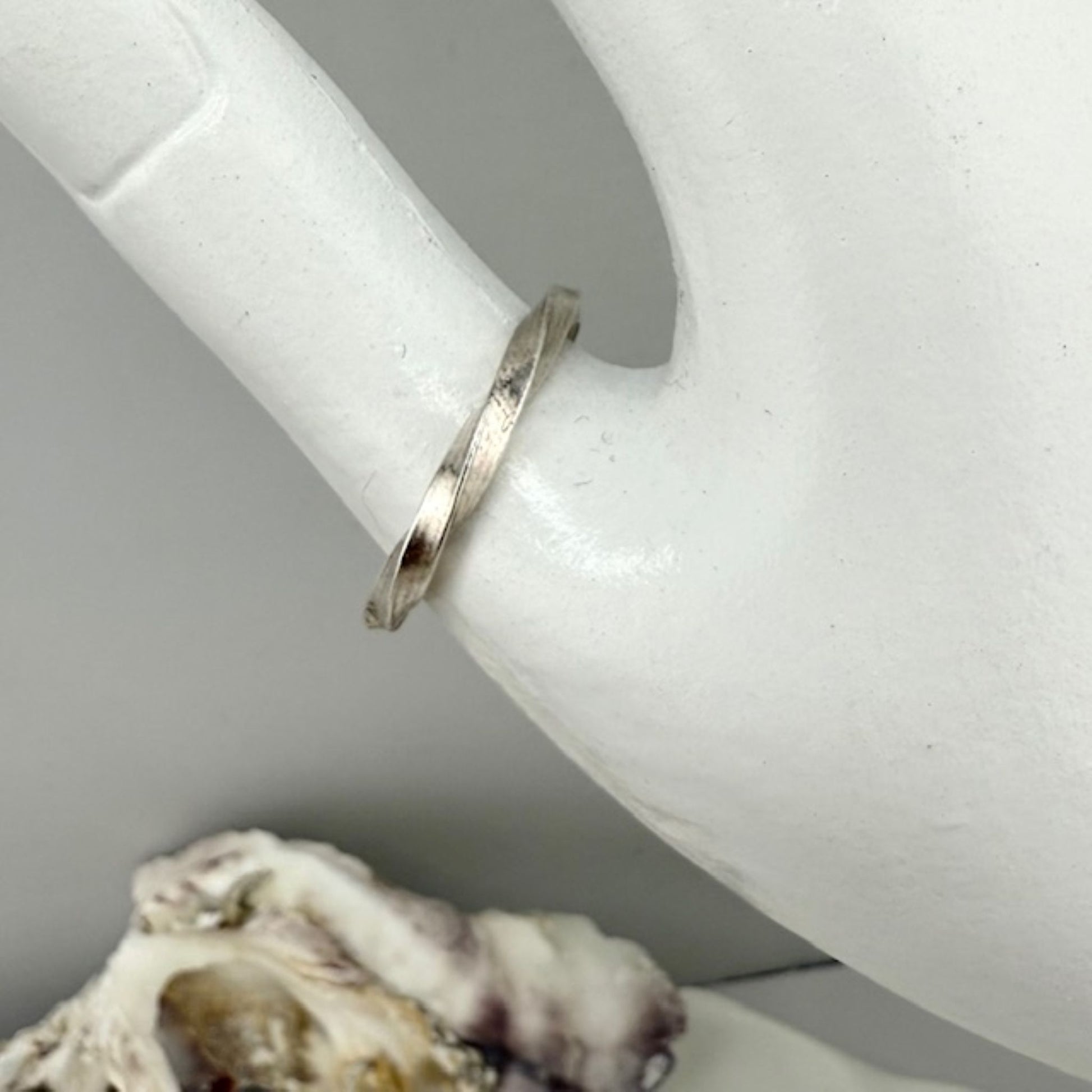 Silver ring on a white display hand with a shell in the foreground