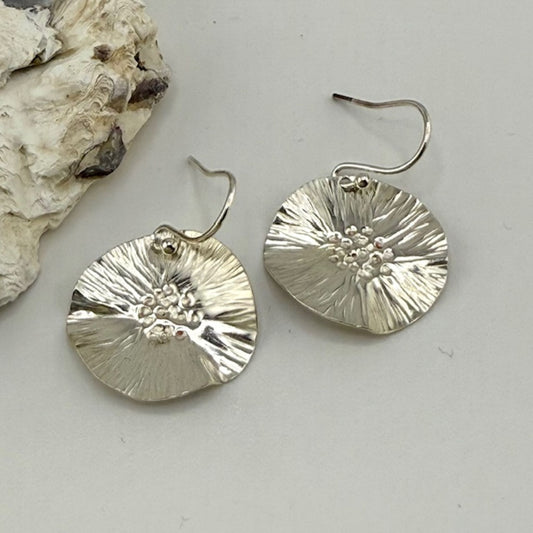 Silver floral earrings on a light gray surface with a natural stone background