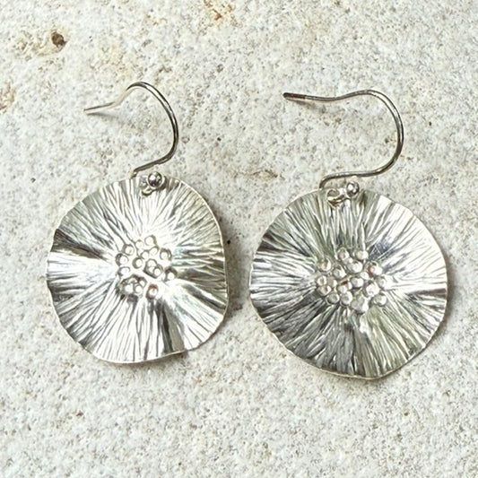 Silver floral earrings on a textured stone surface