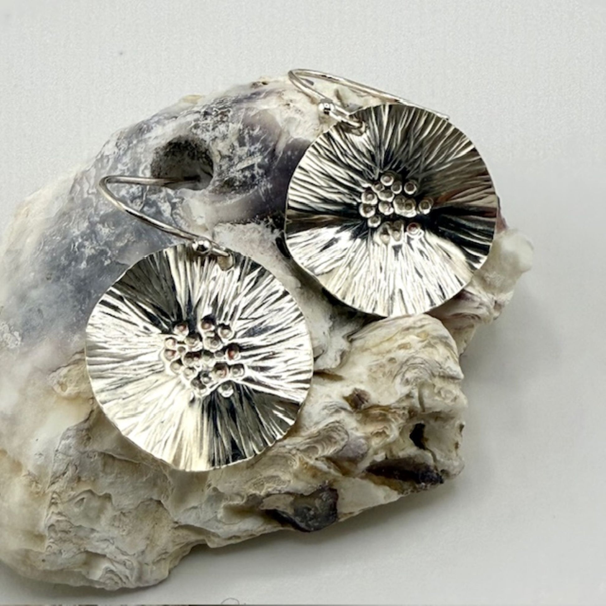 Silver floral earrings on a textured stone surface