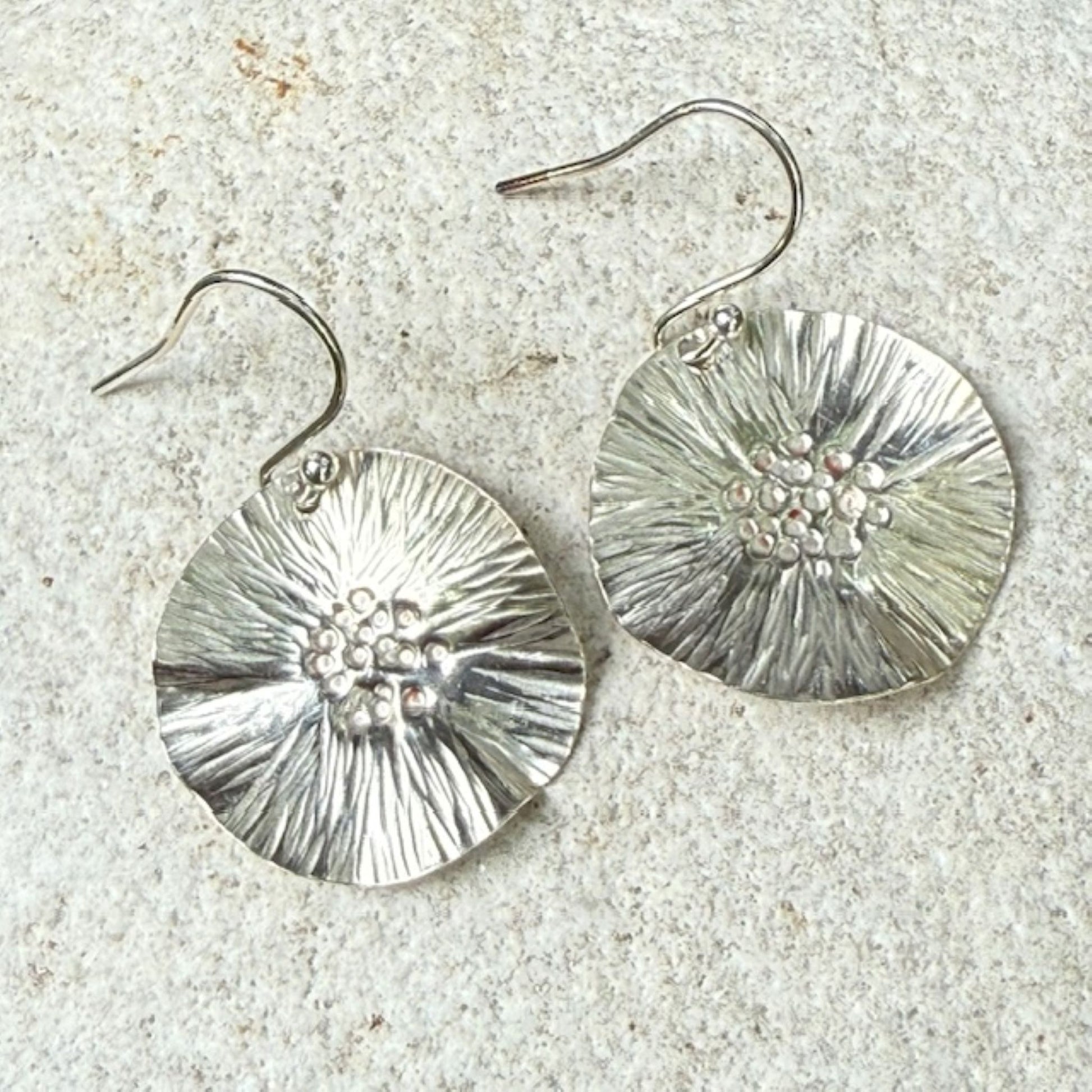 Silver floral earrings on a textured stone surface