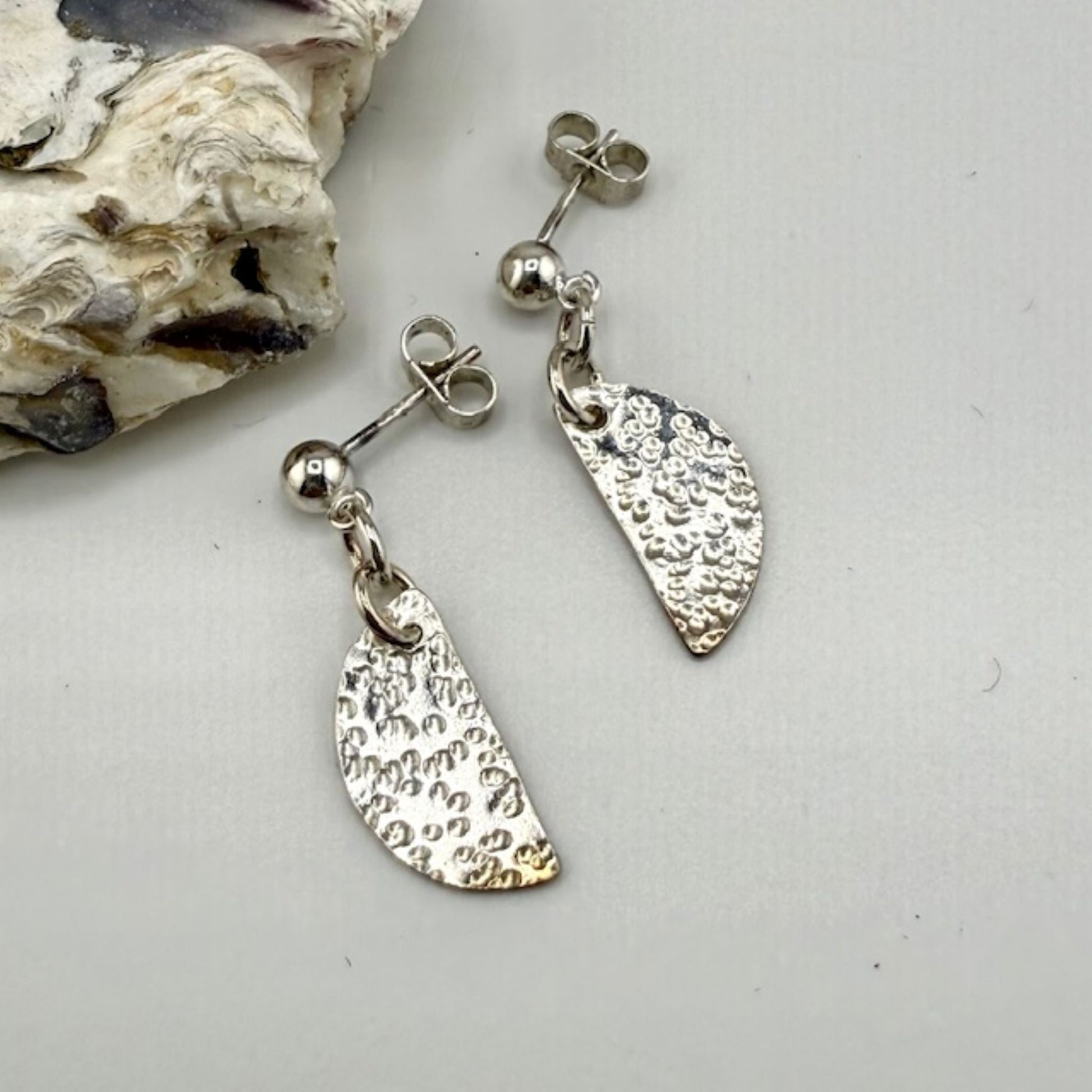Silver half moon stud earrings on a light gray background with a shell.