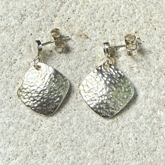 Pair of silver square earrings with textured square pendants on a light gray surface