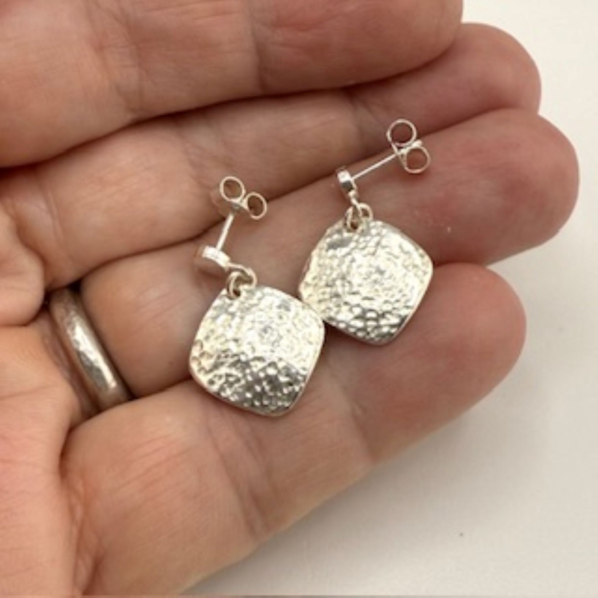 Silver square earrings held in a hand against a white background