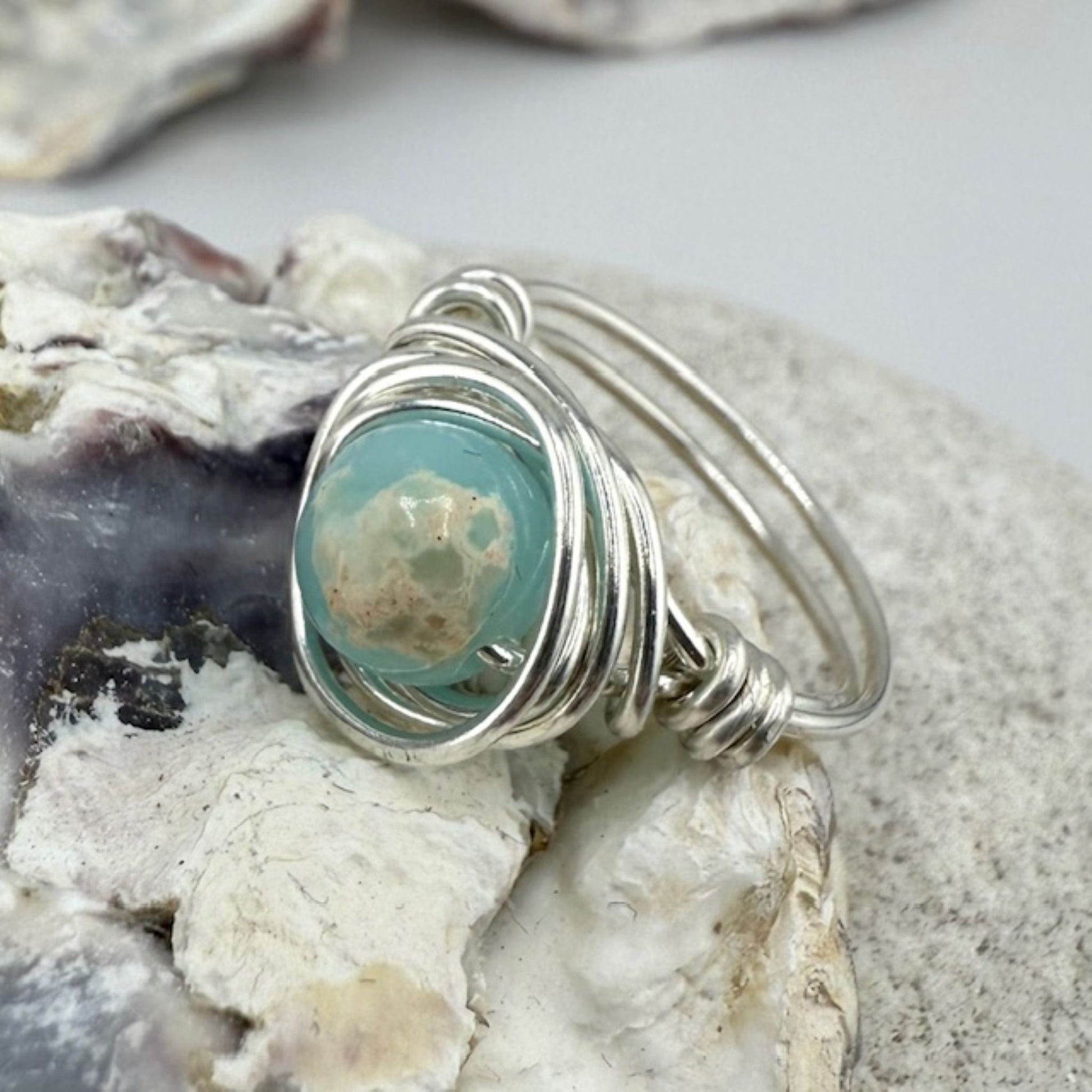 Silver ring with a sea blue green stone on a textured surface