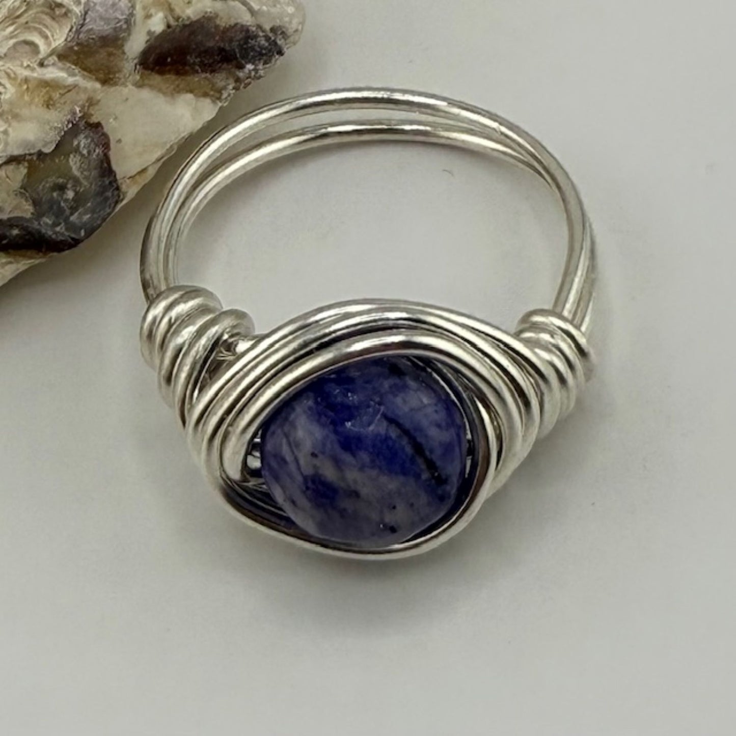 Round blue lapis lazuli gemstone ring wire wrapped in silver on a plain background