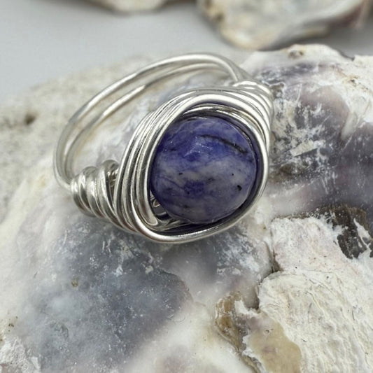 Silver wire-wrapped ring with a purple stone on a textured surface