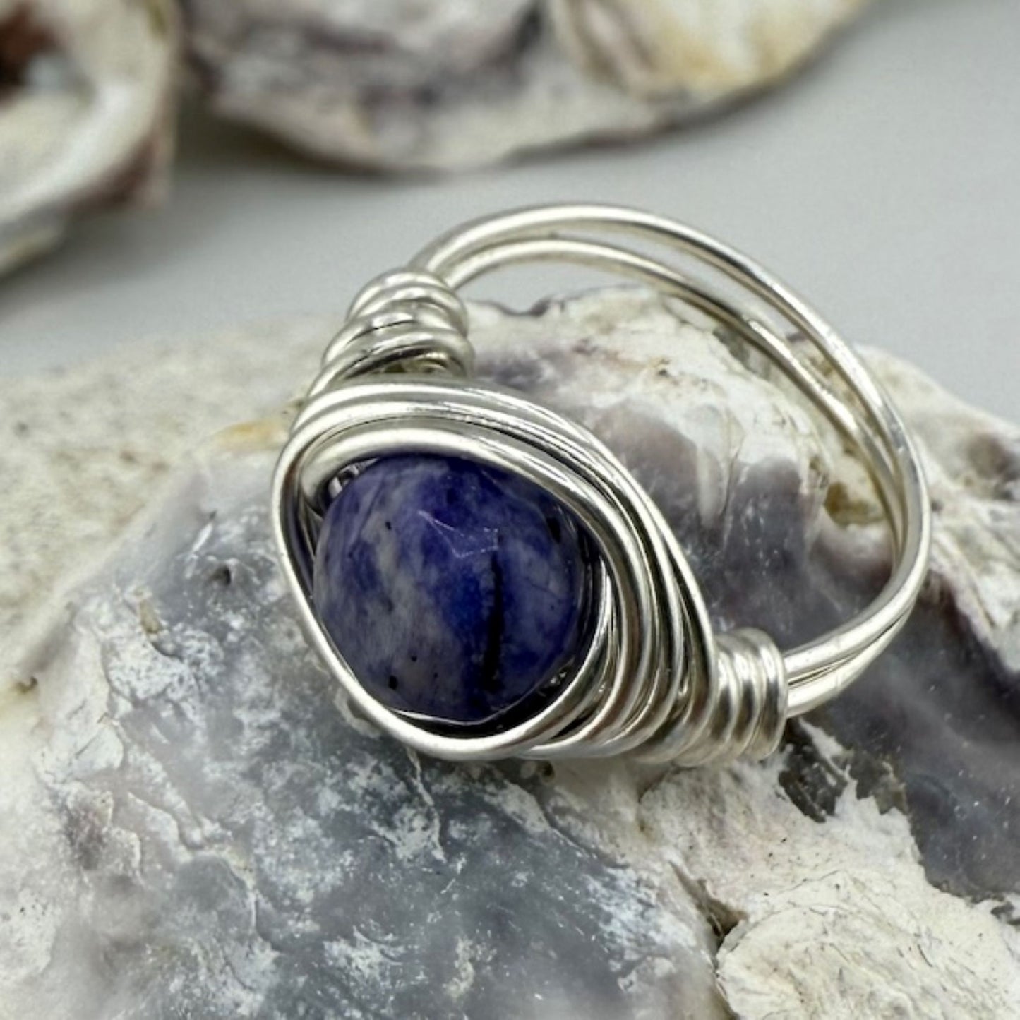 Silver wire-wrapped ring with a blue stone on a rock background
