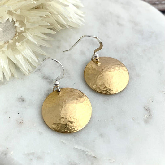 Gold disc earrings on a marble surface with decorative elements.