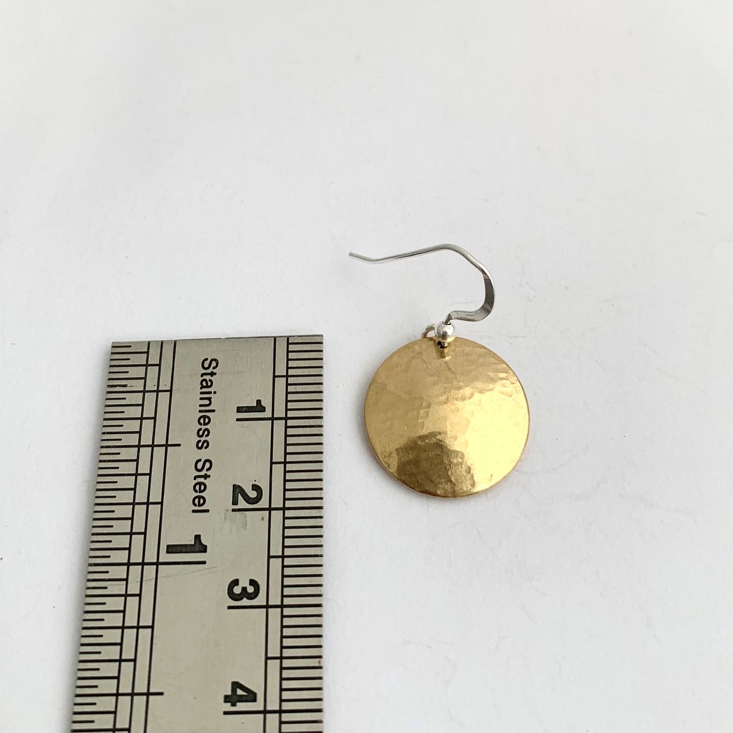 Gold earring next to a ruler on a white background