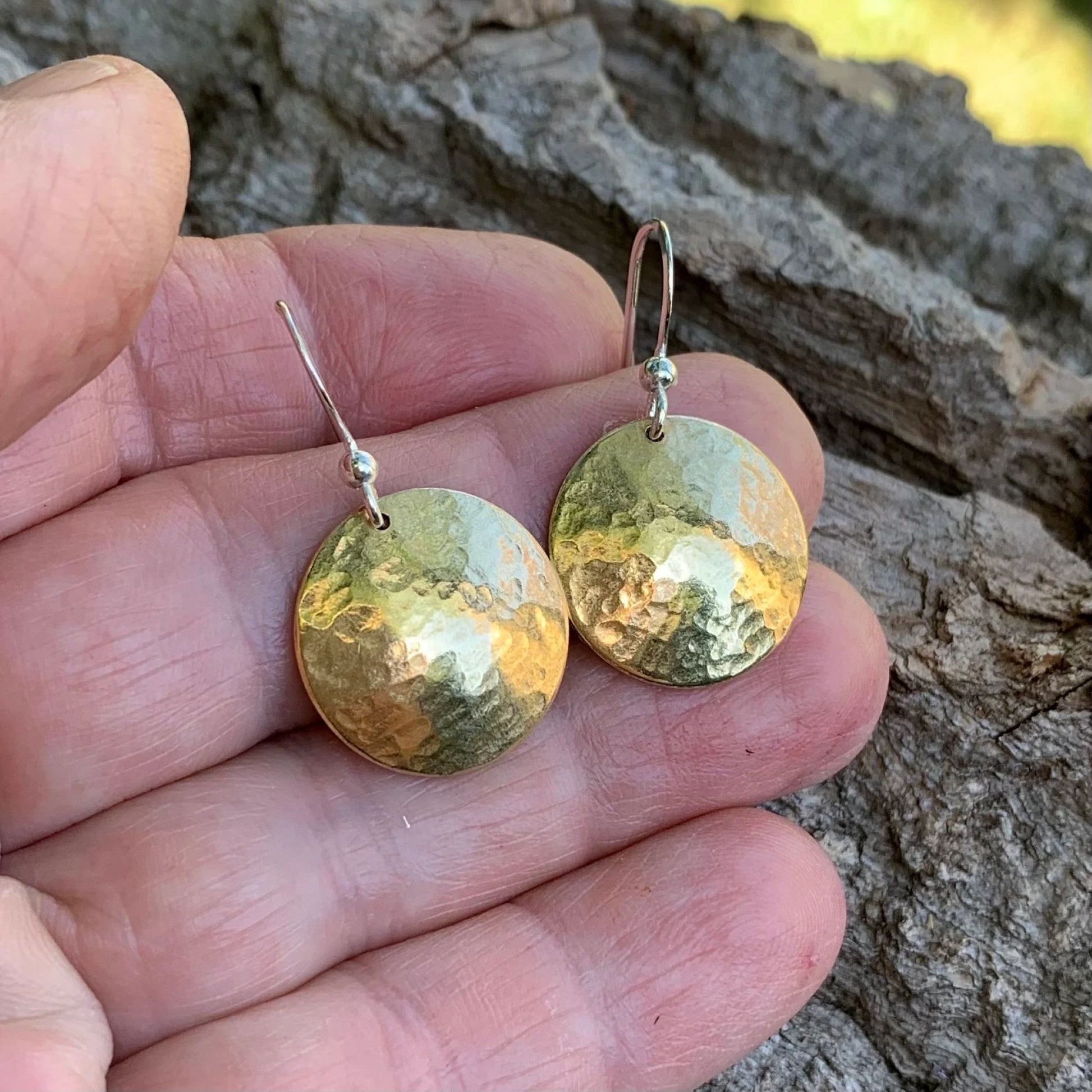 Gold round earrings held between fingers against a natural background