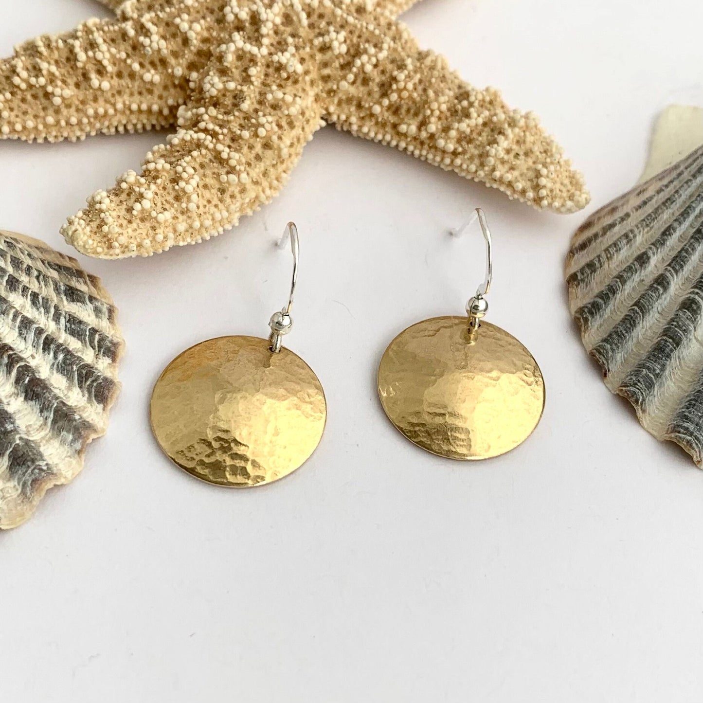 Gold round earrings on a white background with seashells.