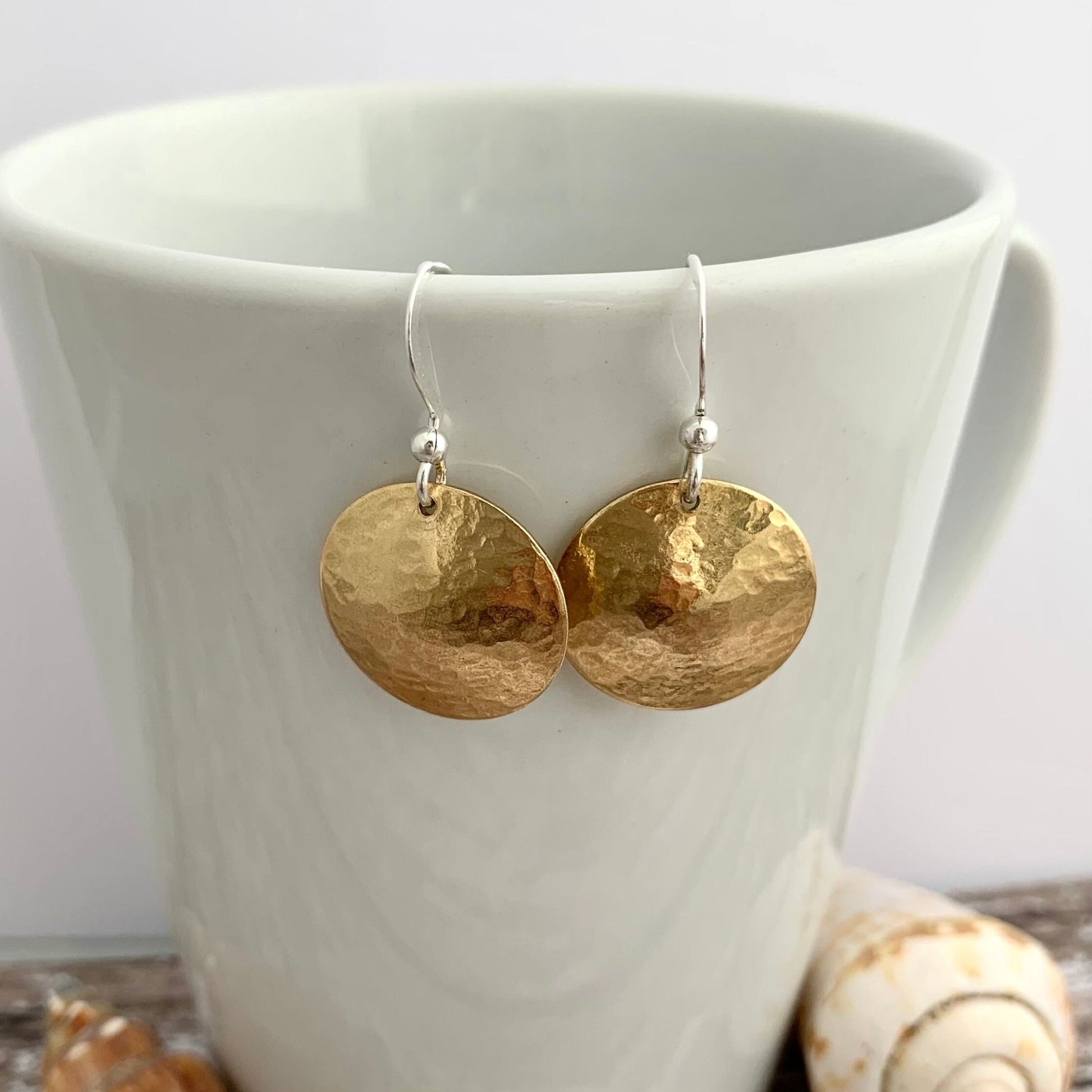 Gold earrings on a white cup with seashells in the background