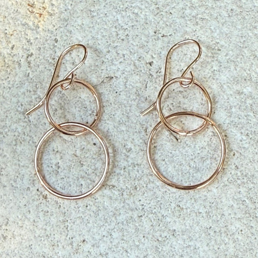 Pair of rose gold hoop earrings on a textured surface