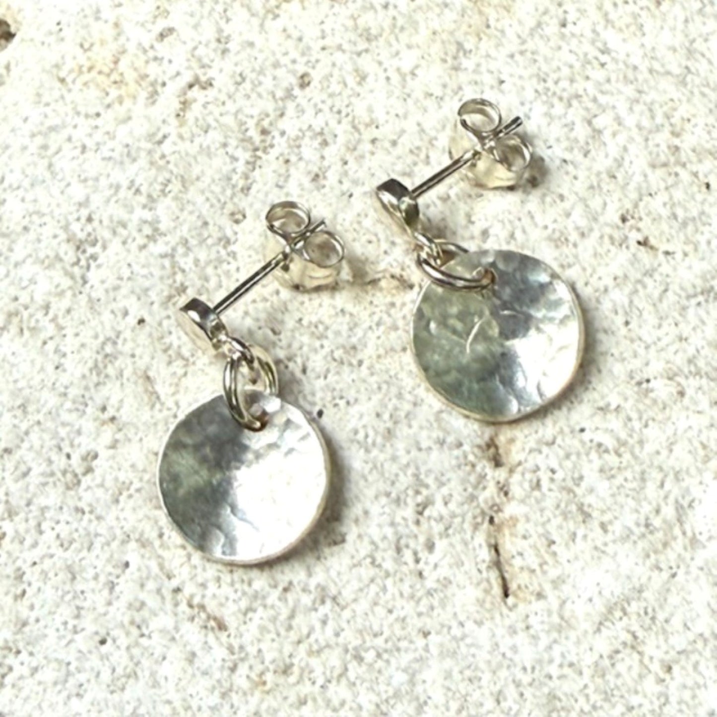 Silver round stud earrings on a textured stone surface