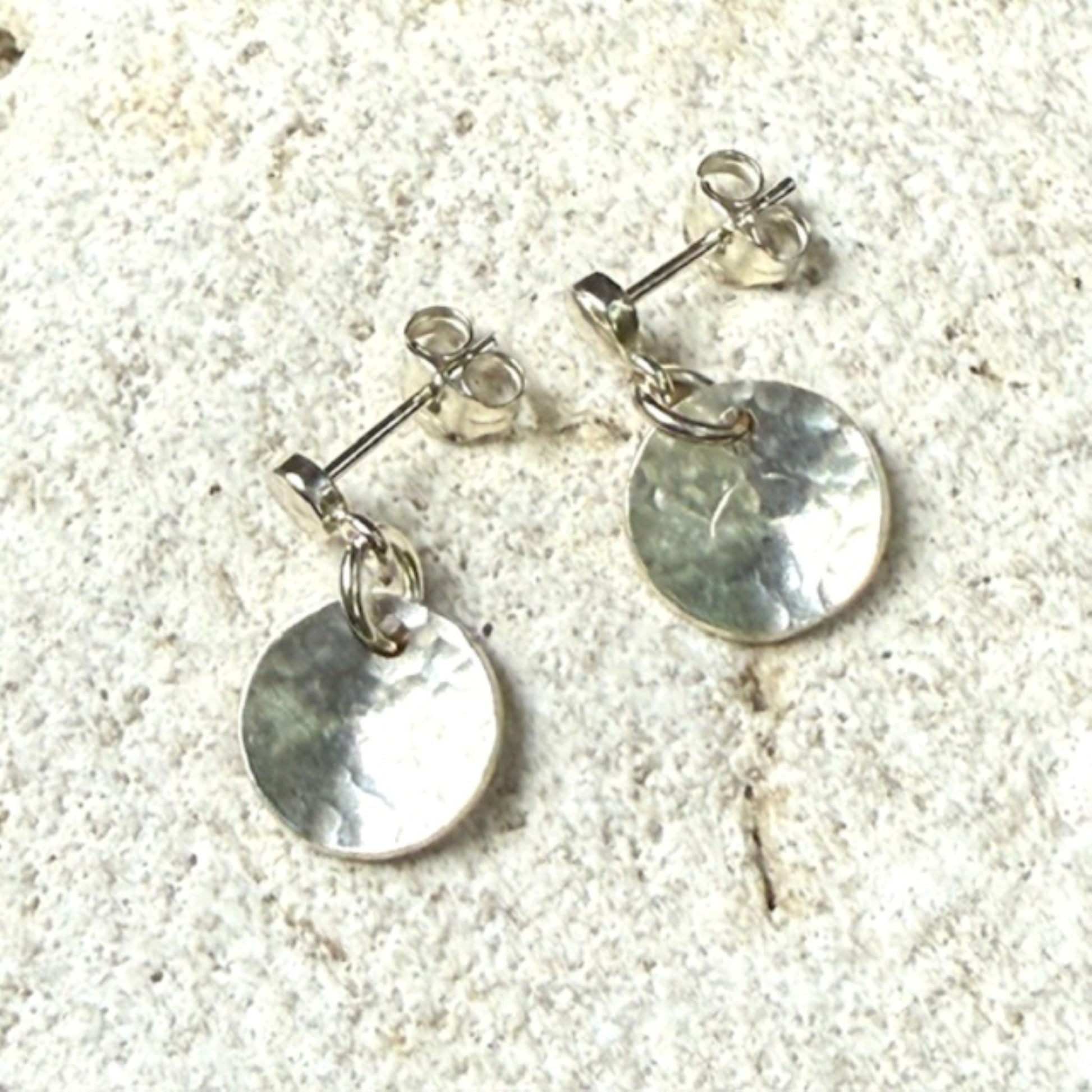 Silver round stud earrings on a textured stone surface