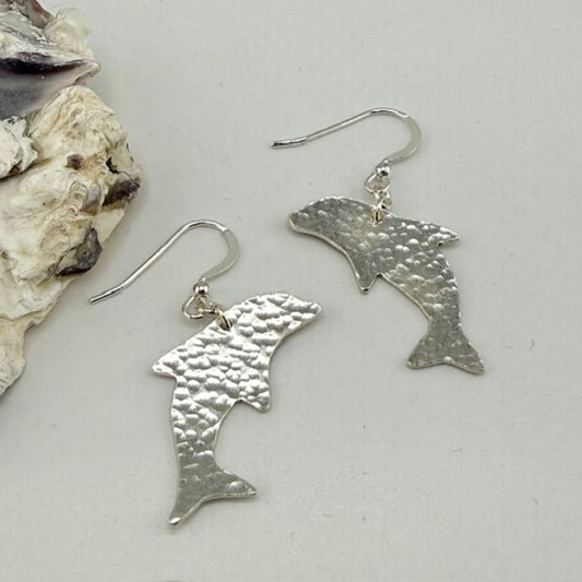 Silver dolphin-shaped earrings on a light gray background with a shell.