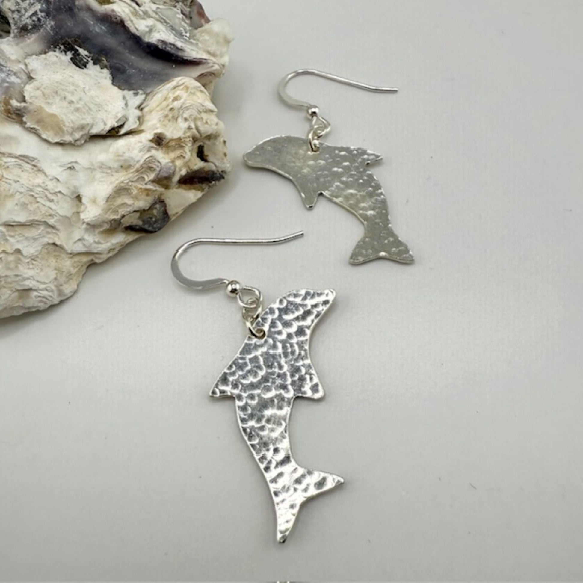 Silver dolphin earrings on a light gray surface with a shell background