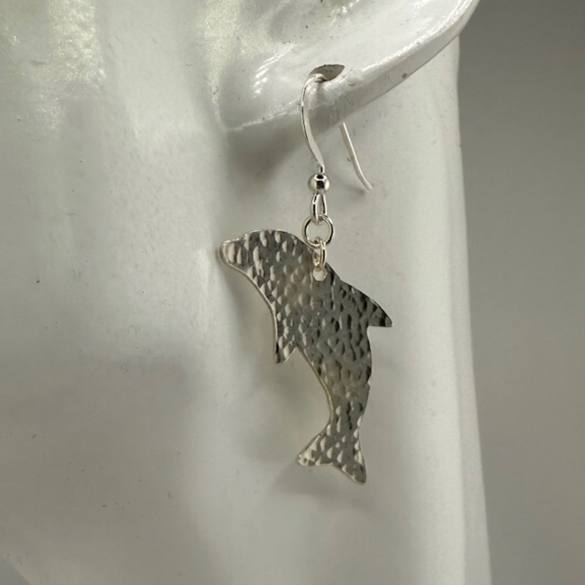 Silver dolphin earrings on a white earring stand.