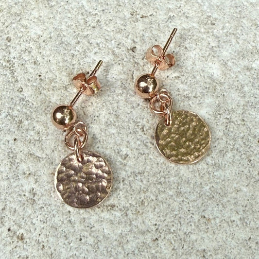 Rose gold stud earrings on a textured stone surface