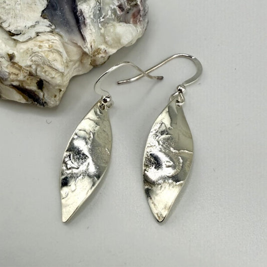 Silver leaf-shaped earrings on a light gray background with a piece of stone.