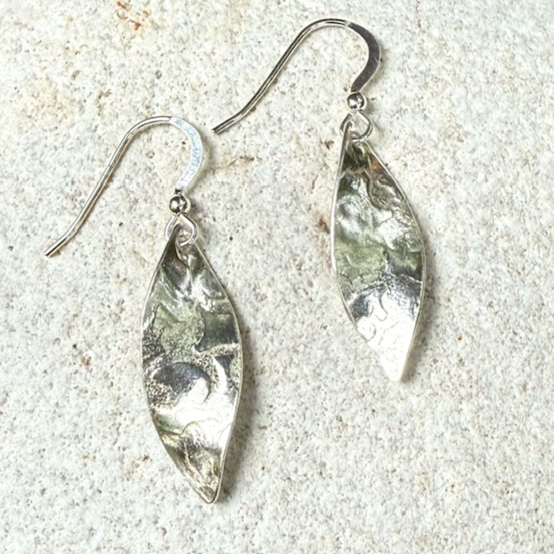 Silver leaf-shaped earrings on a textured stone surface