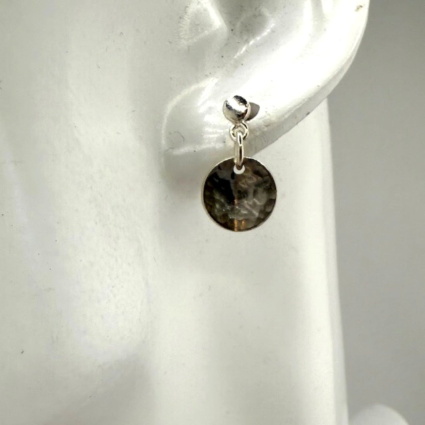 Close-up of an silver disc earring on a white ear display