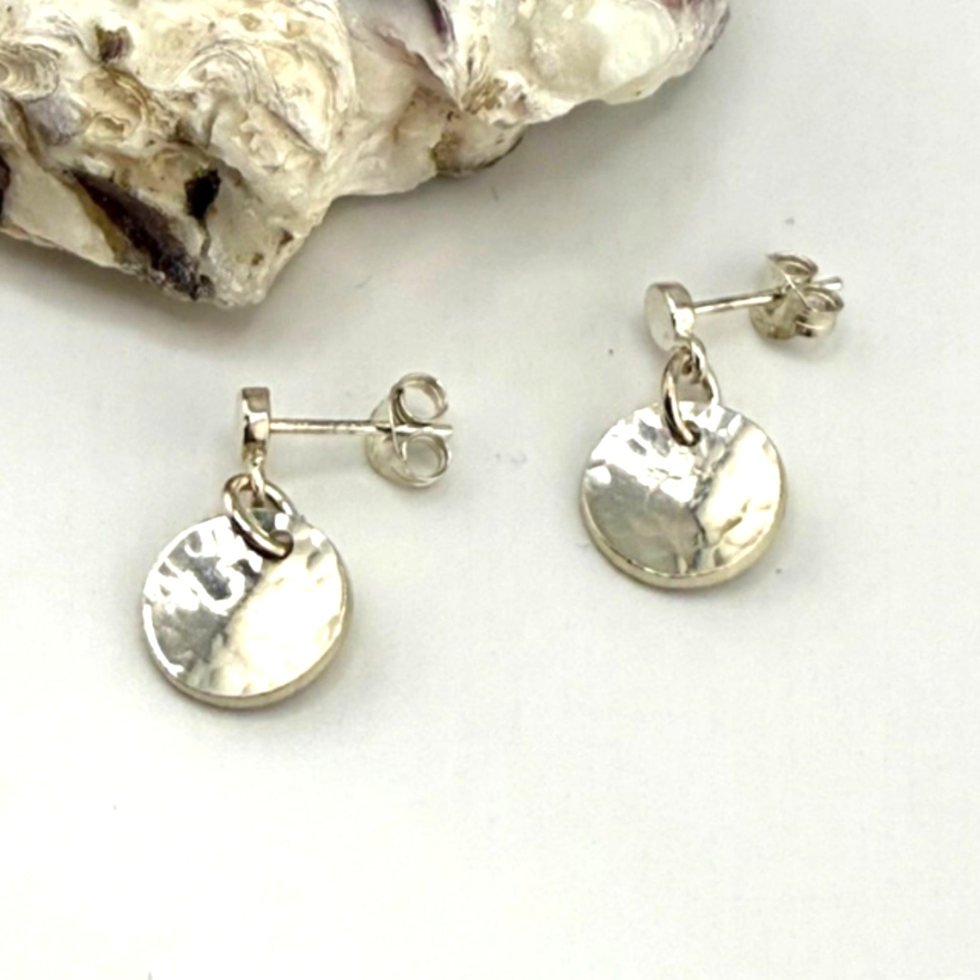 Silver earrings on a white surface with a shell in the background
