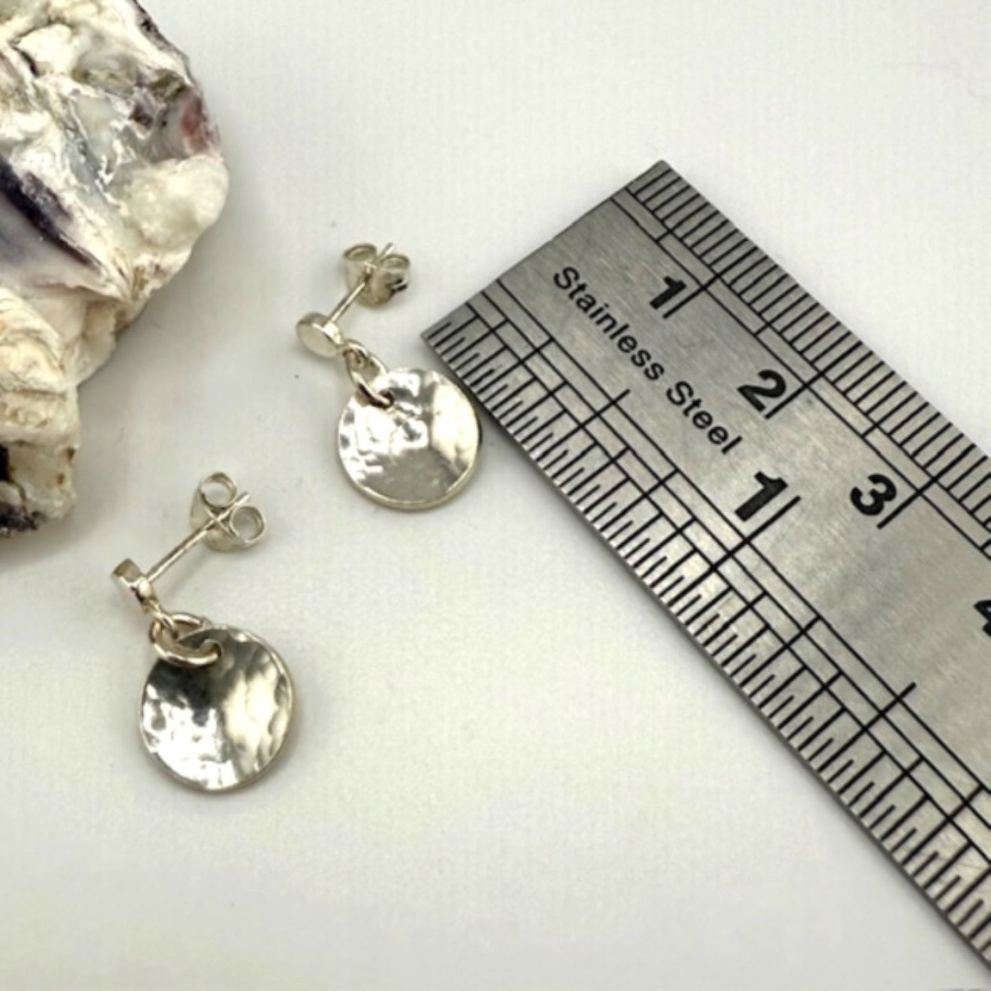 Silver earrings with a ruler for scale on a white background