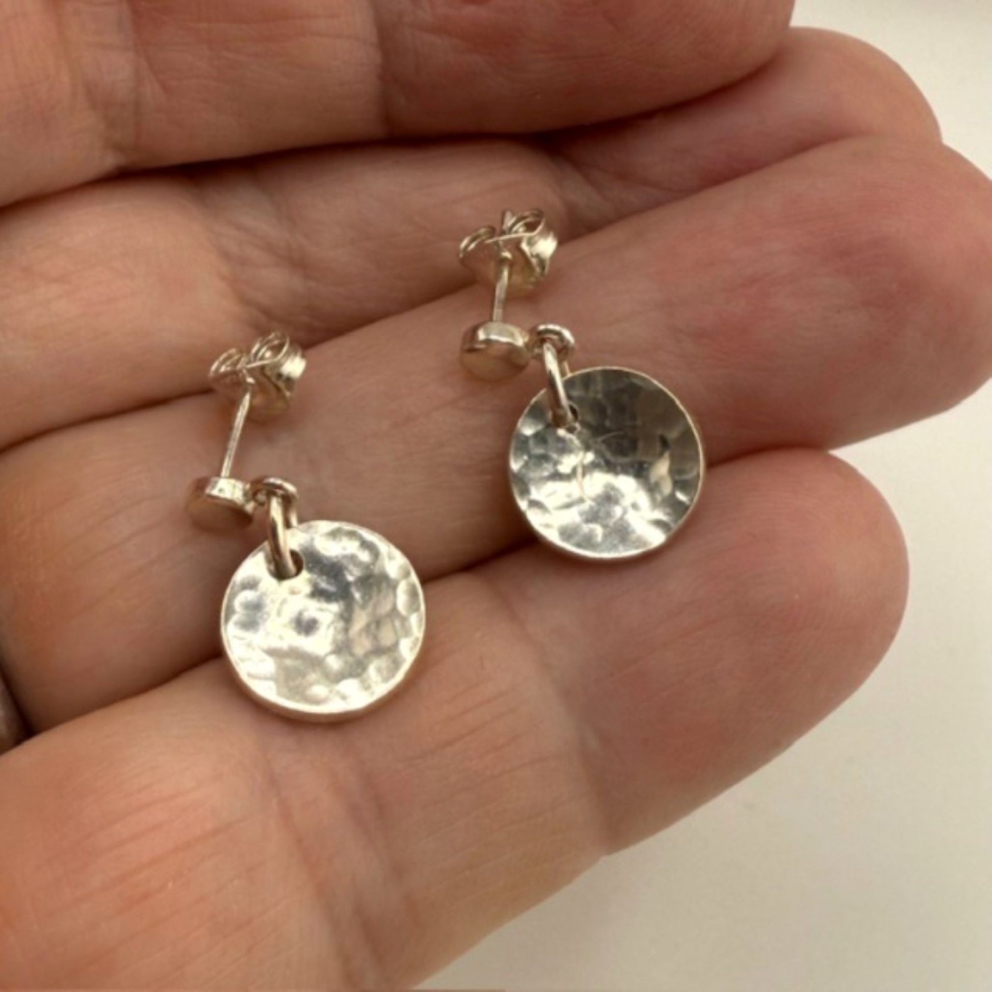 Silver disc earrings held between fingers against a neutral background