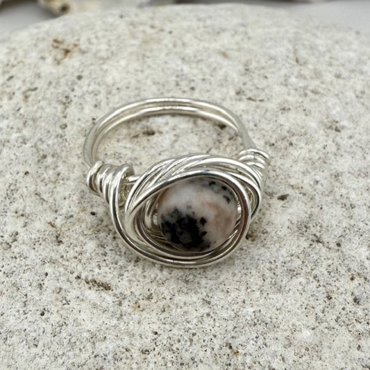 Silver wire-wrapped ring with a central stone on a textured surface