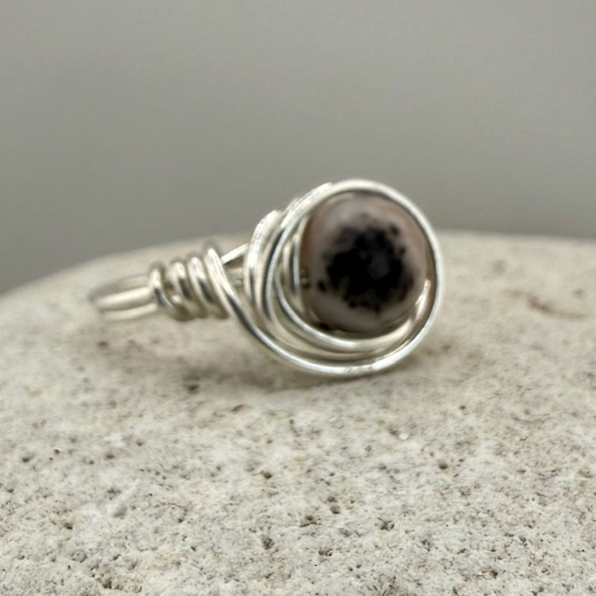 Silver wire-wrapped ring with a pink zebra jasper stone on a textured surface