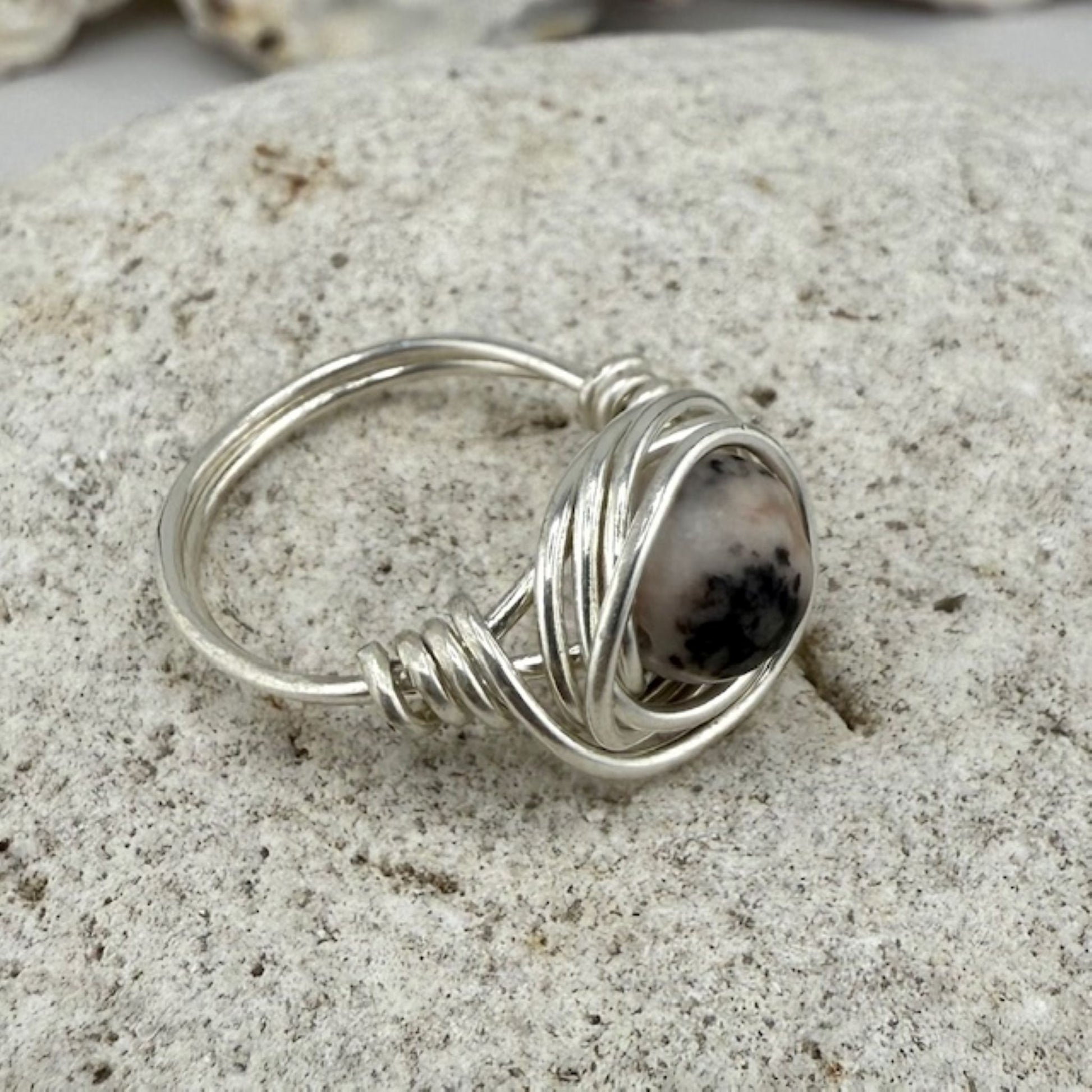Silver wire-wrapped ring with a black and pink gemstone on a stone surface
